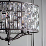 Close-up of Endon Aldwick 8 Light Pendant in dark bronze, showing tiered faceted K5 crystal drum shade and curved arms against a pale panelled wall.