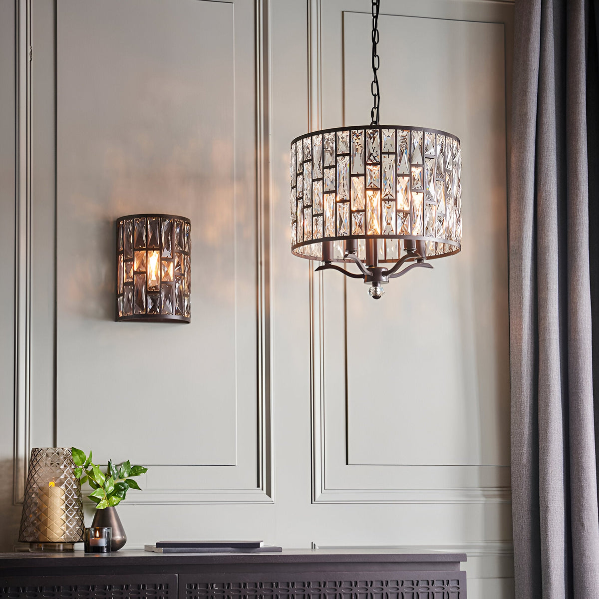 Endon Aldwick wall light in dark bronze with tiered faceted crystals, shown lit beside a matching crystal drum pendant on a panelled wall.