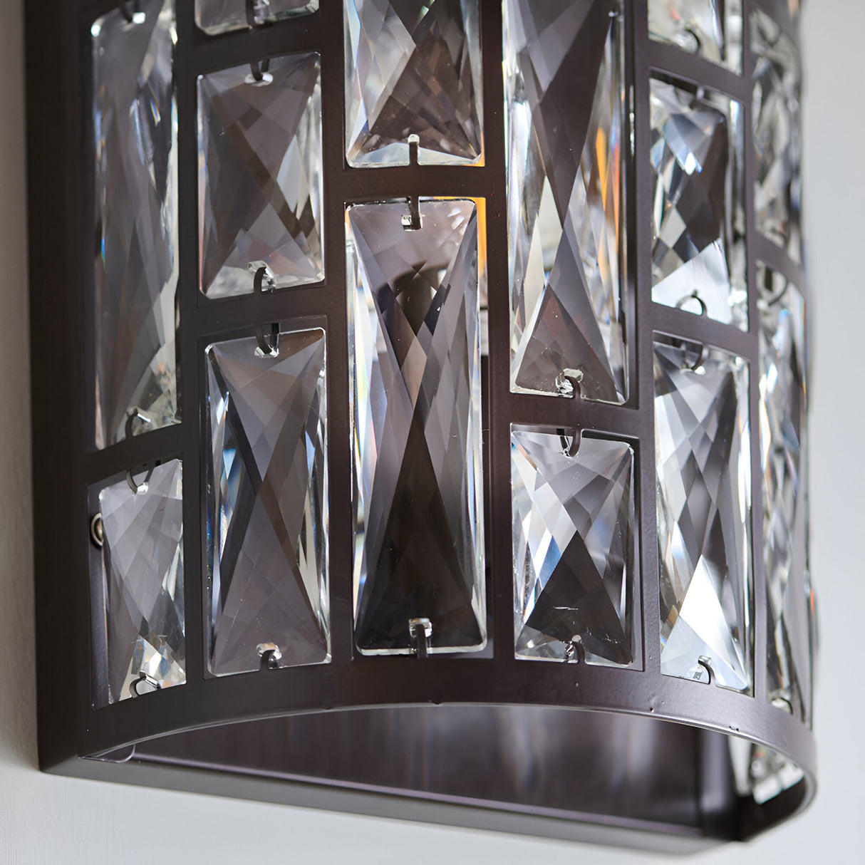 Close-up of Endon Aldwick wall light in dark bronze, showing tiered faceted clear crystals set in a rectangular metal frame against a pale wall.