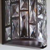 Close-up of Endon Aldwick wall light in dark bronze, showing tiered faceted clear crystals set in a rectangular metal frame against a pale wall.