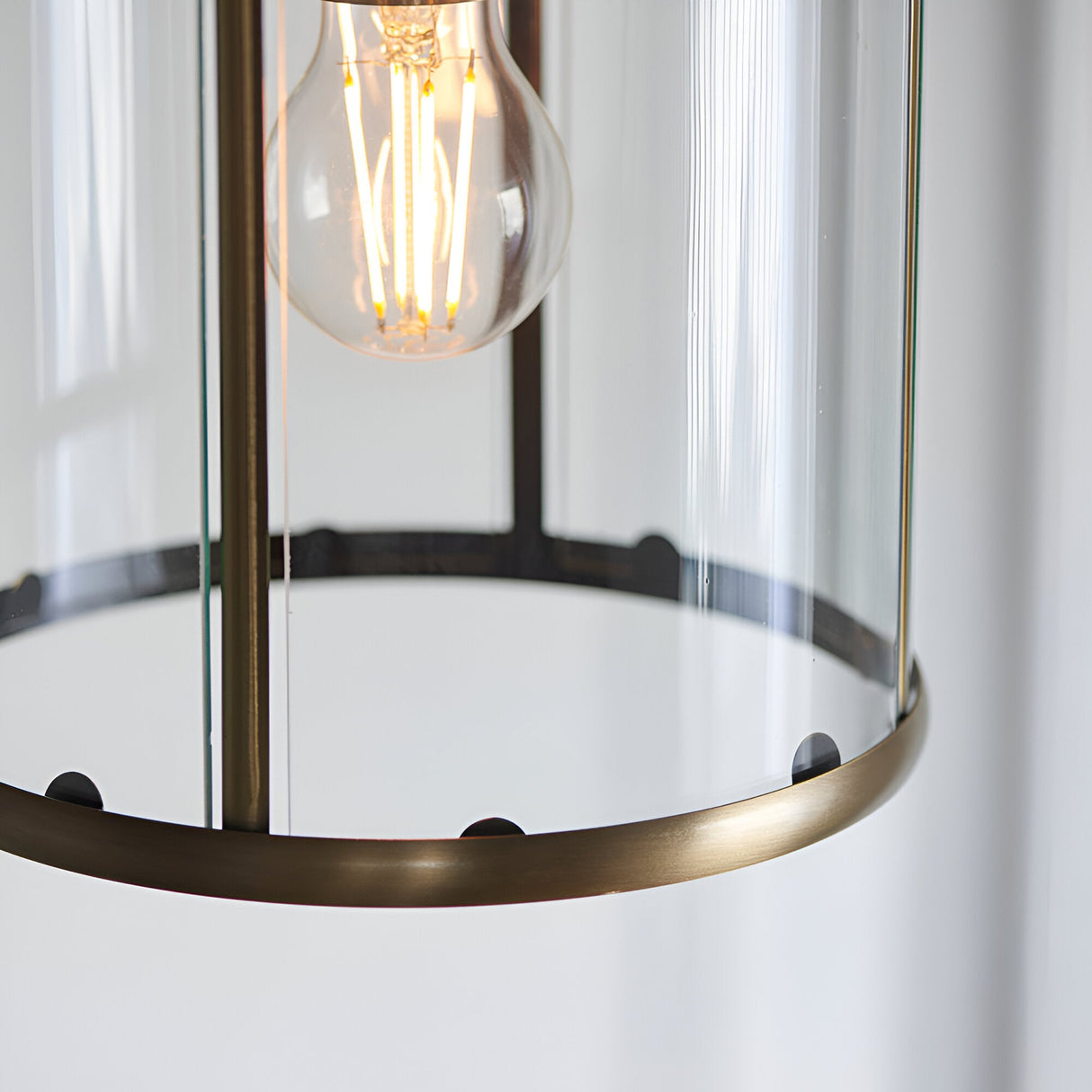 Close-up of the Caldbury Pendant Light in brass, showing its clear glass panels, slim metal frame, and exposed E27 filament bulb.