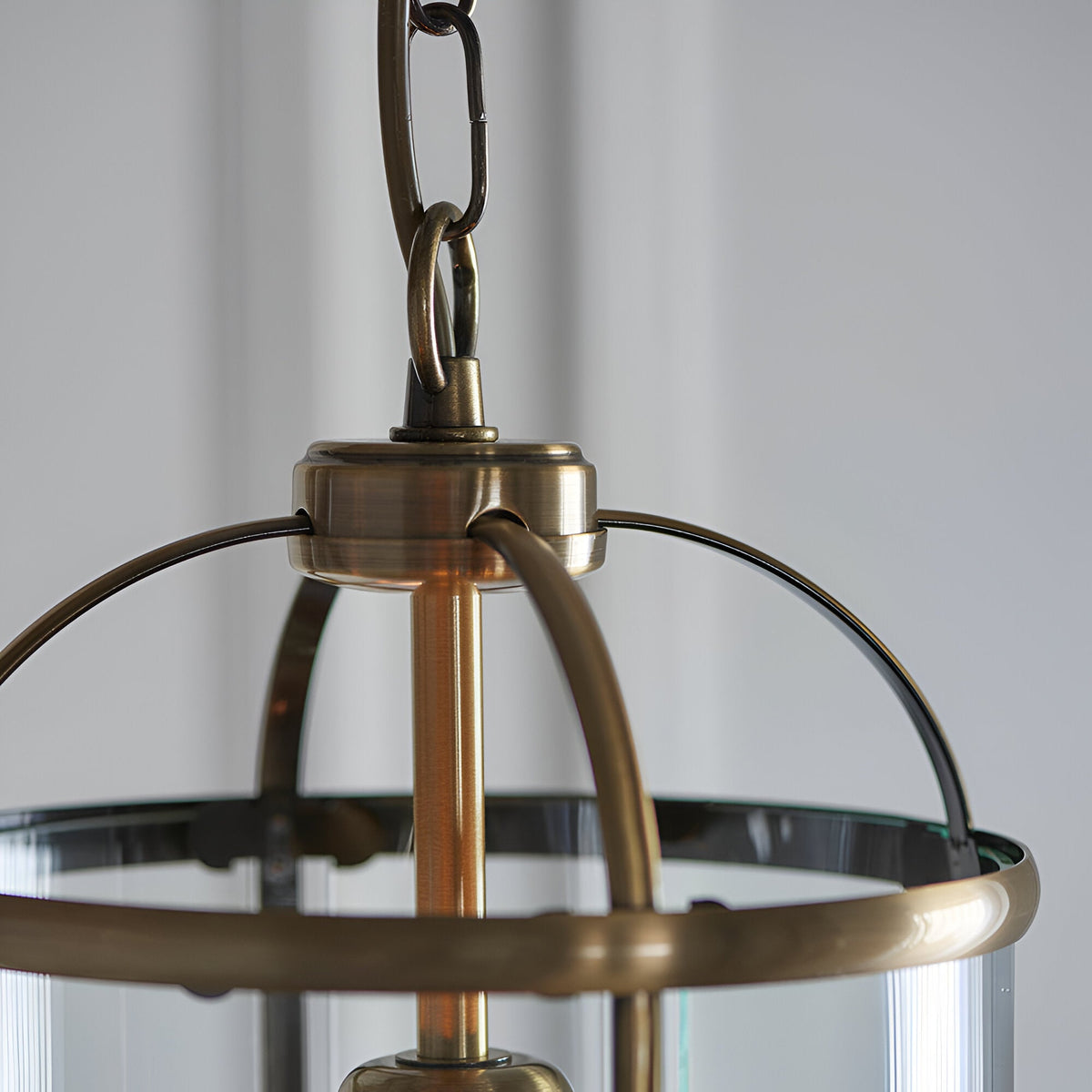 Caldbury Pendant Light in brass, close-up of lantern-style frame with clear glass panels and adjustable chain, on a plain grey background.