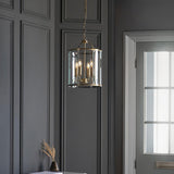 Caldbury 4 Light Pendant in brass with clear glass panels and candle-style bulbs, hanging on a chain against dark panelled walls.