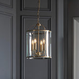 Caldbury 4 Light Pendant in brass with clear glass panels and candle-style bulbs, hung from a chain against dark panelled walls.