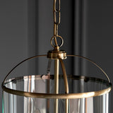 Caldbury 4 Light Pendant in brass, close-up of chain, ring hook and canopy above clear glass panels with metal frame, set against a grey background.