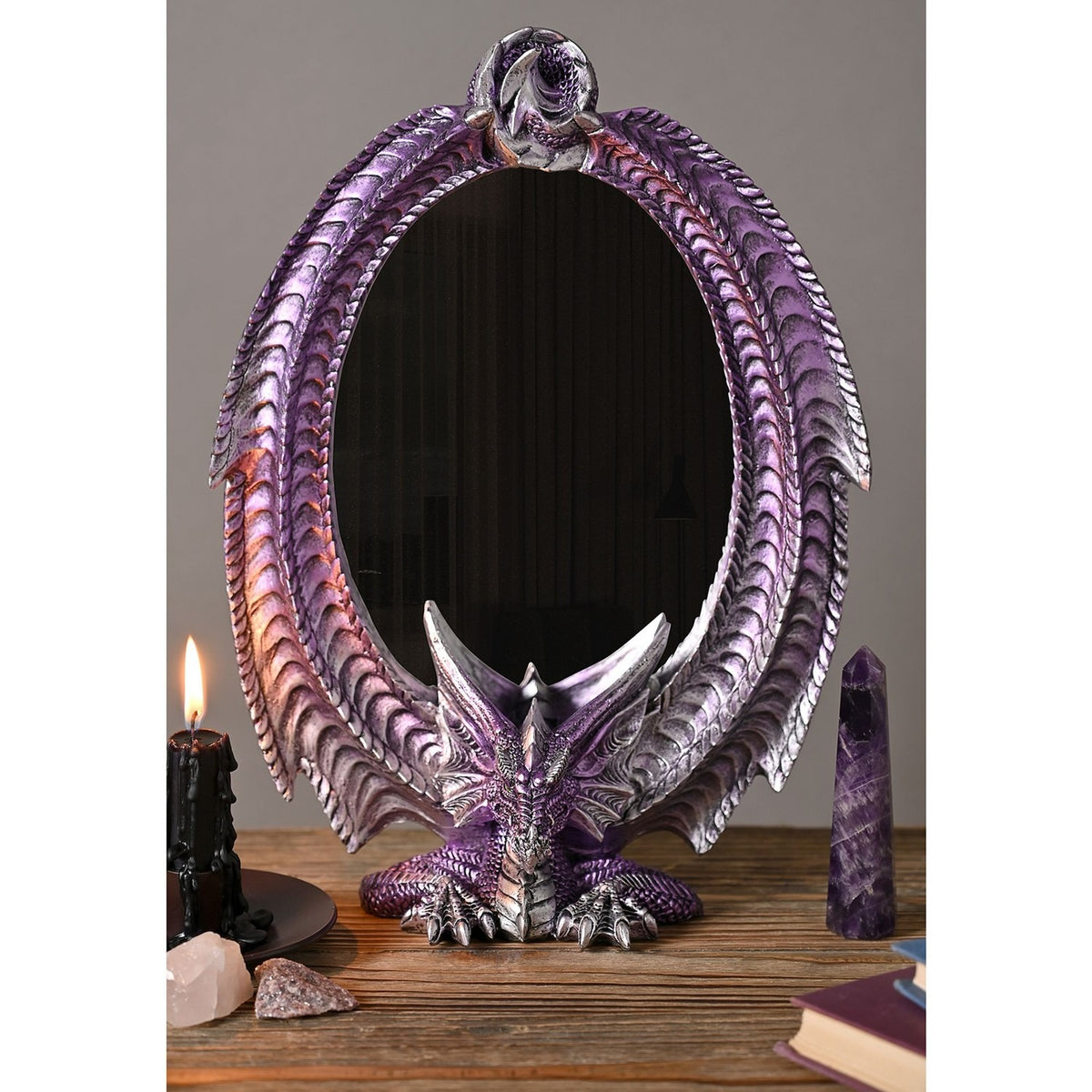 Oval resin mirror with purple metallic finish and silver-highlighted scales, featuring a dragon perched at the base with wings curving up to meet at the top, displayed with candles and crystals.