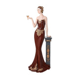 Lola 1920s Lady and Column Resin Figurine 34cm in dark berry, wearing a gold floral trim gown, pearl headband and necklace, raising a coupe glass beside a grey column.