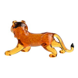 Miniature glass lion figurine in mottled orange glass with paler golden legs and tail, black tail tip, four-legged pose on a plain white background.