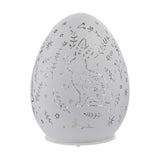 White glass oval Easter egg LED light-up decoration with cut-out rabbit, floral, leaf and star pattern, set on a small white base against a plain background.