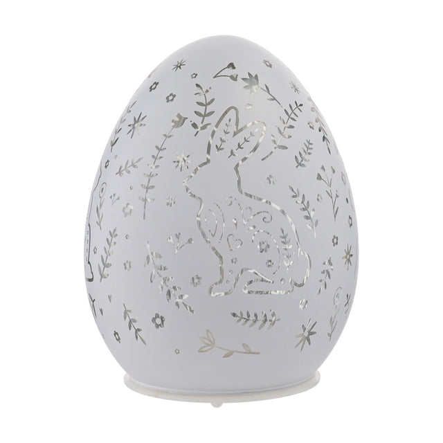 White glass oval Easter egg LED light-up decoration with cut-out rabbit, floral, leaf and star pattern, set on a small white base against a plain background.