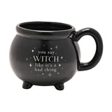 Black ceramic cauldron mug with stubby feet and loop handle, glossy finish with white "you say WITCH like it's a bad thing" text and stars, on a plain white background.
