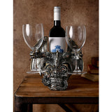 Steampunk Skull & Dragon resin wine and glass holder in silver, with a winged dragon over a gears-and-cogs skull, holding two wine glasses and a bottle on a wooden table.