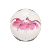 Round clear glass paperweight with an encased pink flower design, curled petal tips, and a clear centre bead, shown on a plain white background.