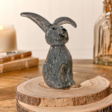 Floppy Eared Sitting Rabbit glass figurine in flecked grey, with tall upright ears, black eyes and nose, displayed on a wood slice indoors.