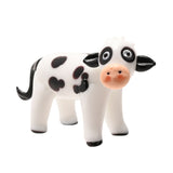 Standing black spotted cow glass miniature figurine in milky white glass with a peach muzzle, black ears, ringed eyes, and curved black tail, shown on a plain white background.