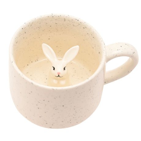 Speckled cream ceramic mug with a loop handle, viewed from above showing a hidden 3D white bunny figure with tall ears inside the base, on a plain white background.