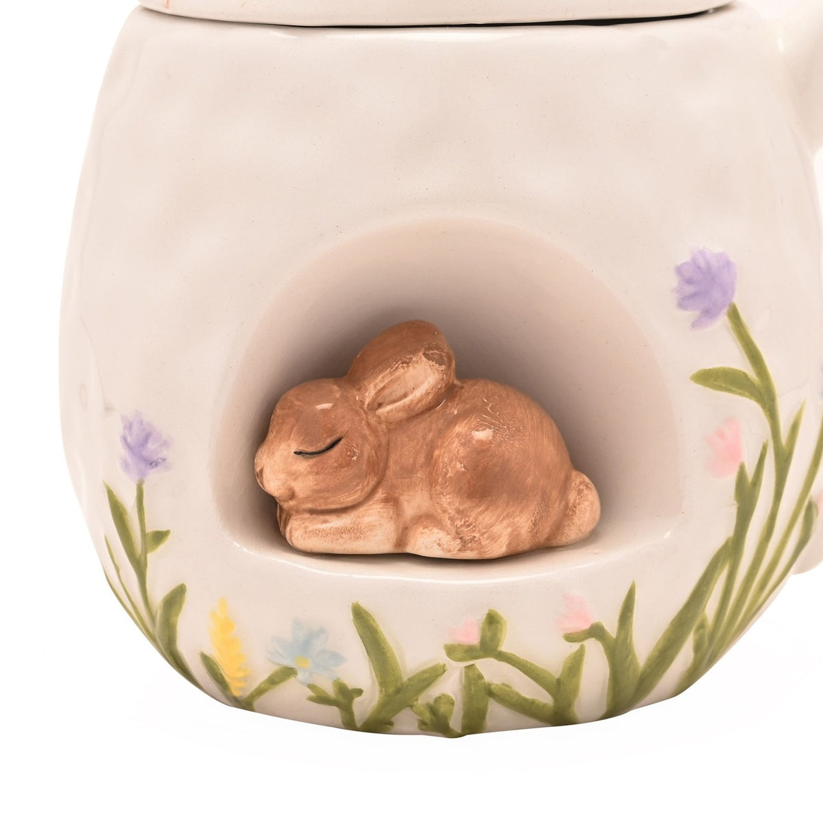 Close-up of the white ceramic Easter mug showing a 3D sleeping bunny nestled in an arched front nook, with hand-painted grass and pastel flowers along the base.