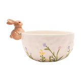 White round ceramic bowl with a 3D sandy brown bunny perched on the rim and pastel wild flowers in lilac, pink, yellow and blue across the front, on a plain background.