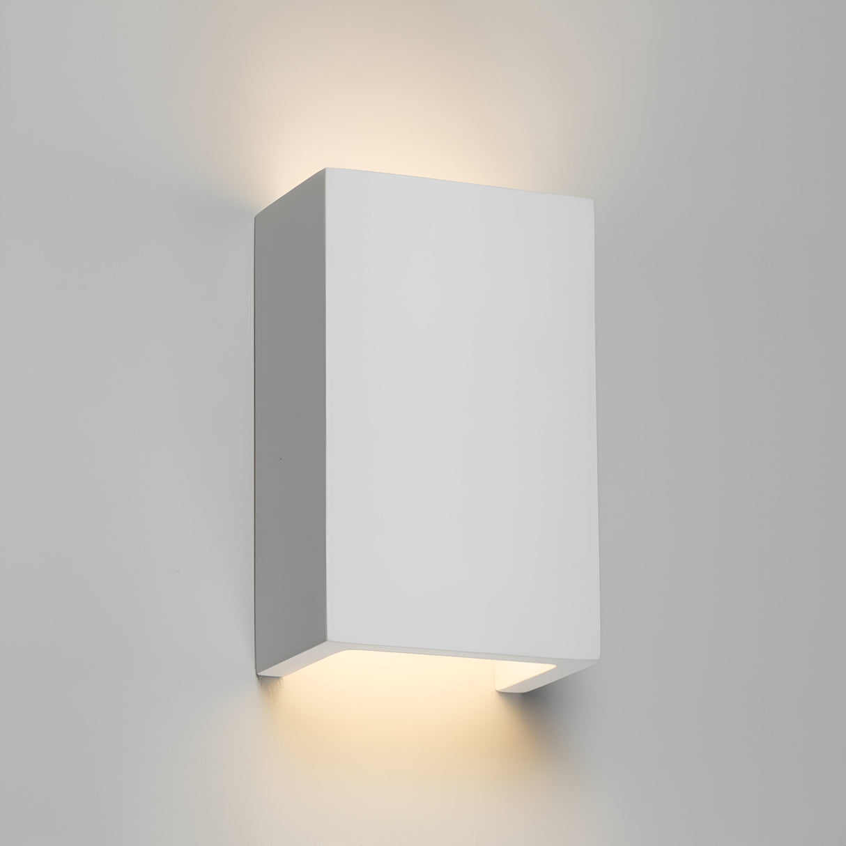 The Cuboid Up And Down Plaster Wall Light is a minimalist and modern wall sconce made from gypsum plaster that emits a soft, warm light both upward and downward, casting a gentle glow on the surrounding wall. It features clean lines and a rectangular shape, perfect for creating sleek ambient lighting with a contemporary appearance.