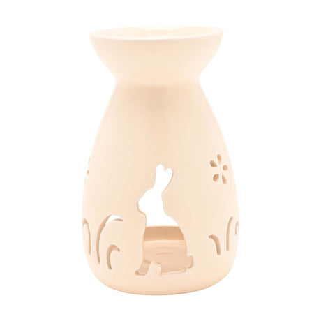 Cream ceramic wax melt burner with a rounded vase shape, featuring a cut-out bunny silhouette, flowers, and grass details, set against a plain white background.