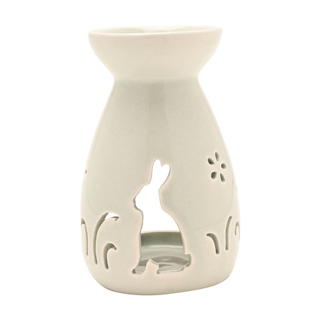 Ceramic wax melt burner in white with a cut-out sitting bunny, flowers, and grass silhouettes, featuring a rounded vase-shaped base and wide top bowl, on a plain background.