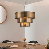Endon Carlwick tiered pendant in antique brass, three stacked cylindrical steel shades on a chain, hung above a dining table beside a round mirror.