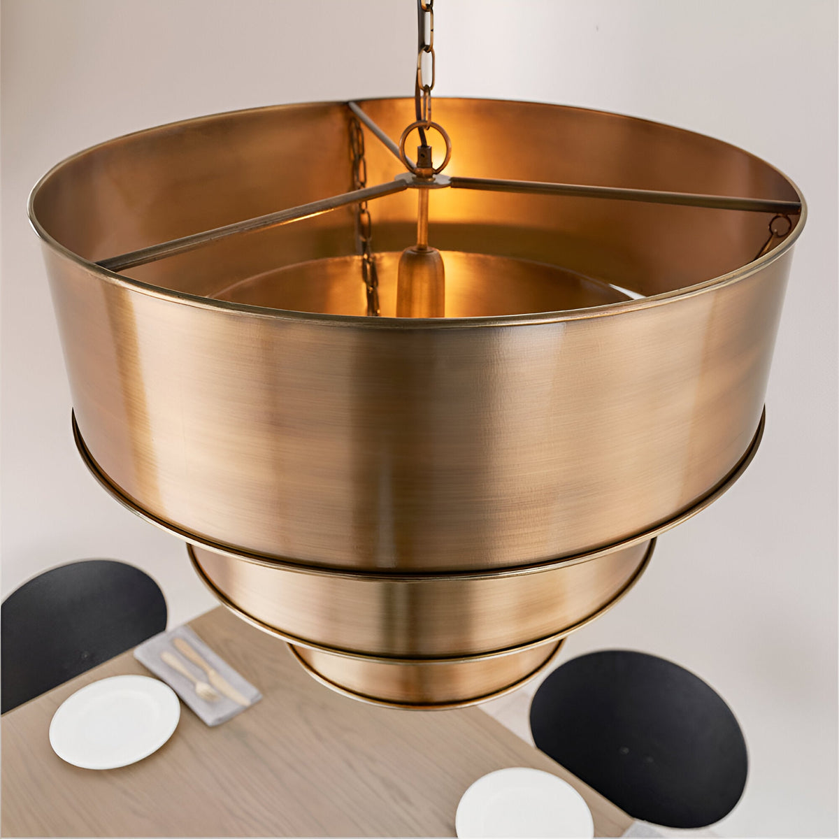 Endon Carlwick tiered pendant light in aged brass, shown from above with stacked cylindrical steel shades on a chain over a dining table.
