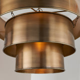 Close-up of the Endon Carlwick tiered pendant showing three stacked cylindrical steel shades in an aged antique brass finish, suspended on metal chains.