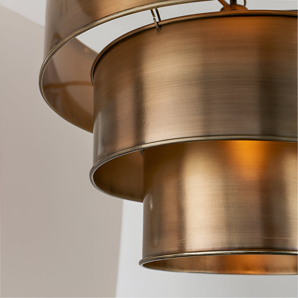 Close-up of the Endon Carlwick tiered pendant showing three stacked cylindrical shades in aged antique brass with a warm internal glow.