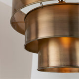 Close-up of the Endon Carlwick tiered pendant showing three stacked cylindrical shades in aged antique brass with a warm internal glow.