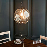 Endon Carldon hexagonal glass pendant in antique brass, illuminated over a wooden dining table against a dark panelled wall.