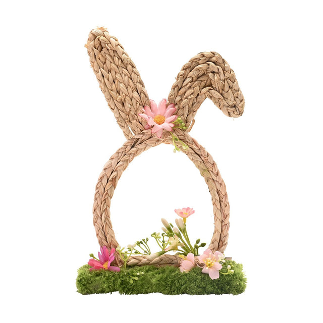Faux flower bunny ears decoration with natural braided ears and egg-shaped loop, pink daisy accent, and faux blooms on a mossy green base, set against a white background.