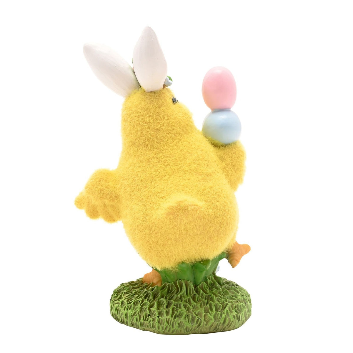Yellow resin Easter chick figurine with white bunny ears, balancing pink and blue painted eggs on its wing, standing on a green grass base against a plain white background.
