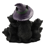 Black resin tealight candle holder showing five textured black cats gathered around a cauldron, viewed from behind with the largest cat wearing a purple witch's hat, on a white background.