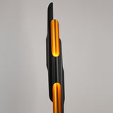 The Stealth 6 Light Floor Lamp in brass and black features a modern vertical design with curved, overlapping shapes. Cut-out sections emit a warm yellow-orange glow, making it perfect for adding stylish, contemporary lighting to any room.