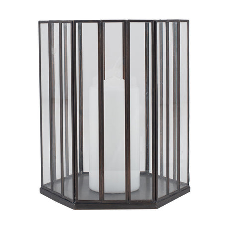 Hexagonal candle lantern with vertical glass panels and dark antique brass frame, holding a white pillar candle, shown on a plain white background.