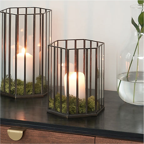 Antique Brass & Glass Hexagonal Lantern (23cm), smaller size shown beside a larger version on a dark sideboard, glass panels with lit pillar candle and moss inside.