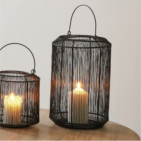 Matt Black Iron Wire Medium Lantern, 34cm, with domed wire cage, arched carry handle and lit candle inside, shown on a wooden table beside a smaller matching lantern.