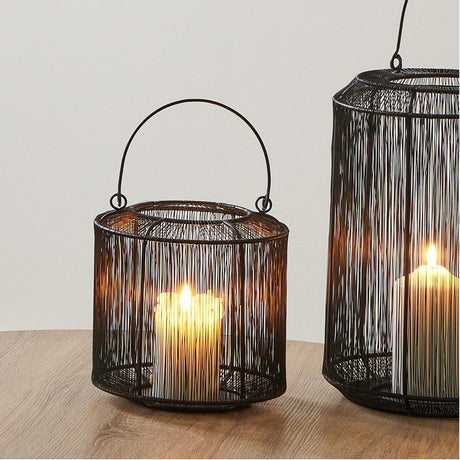 Matt Black Iron Wire Small Lantern - 20cm, a round wire candle lantern with domed top and curved carry handle, shown lit on a wooden surface beside a larger matching lantern.
