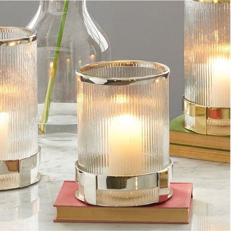 Silver Stainless Steel & Clear Textured Glass Hurricane Lamp, 21cm, with a lit candle, shown on a marble surface beside a book and glass carafe.
