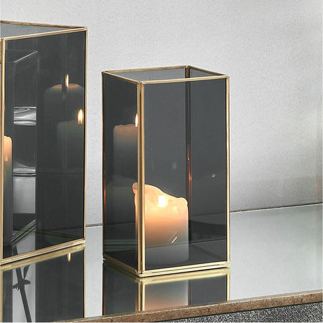 Brass & Smoked Glass Panelled Medium Hurricane Lamp, 26cm, with a lit candle inside, shown on a mirrored surface with a matching lamp reflected alongside.