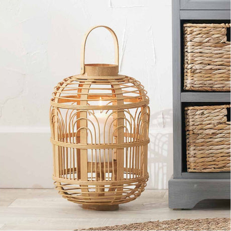 Natural bamboo cage lantern, 38cm, with domed lid, arched detailing and top handle, holding a lit glass candle, shown beside woven storage baskets.