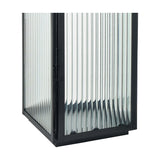 Close-up of a black iron candle lantern with vertical ribbed glass panels and a black base, shown against a plain white background.
