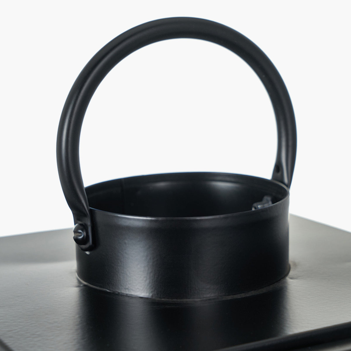 Close-up of a black iron lantern's arched handle and rim, showing the riveted joint and cylindrical top edge against a plain white background.