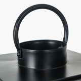 Close-up of a black iron lantern's arched handle and rim, showing the riveted joint and cylindrical top edge against a plain white background.