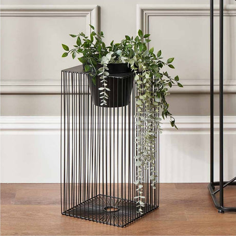 Black Iron Strut Planter, 54cm tall, a tall square wire-frame stand with a black pot holding trailing greenery, shown in a room against a panelled wall.