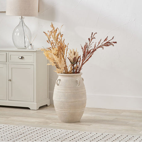 Grey wash fibrestone ribbed large floor vase, 55cm, with side handles, holding dried foliage stems beside a light grey sideboard in a living room setting.