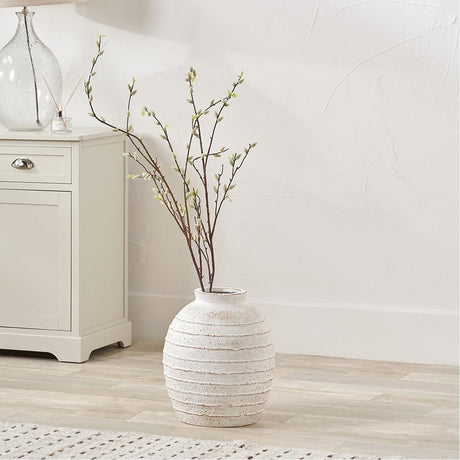 White Wash Fibrestone Decorative Ribbed Vase, 38cm, with textured white finish holding budding branches, styled on a wooden floor beside a cream cabinet.