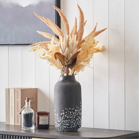 Etna Black & White Glass Vase, 32cm, with mottled speckled base, holding dried pampas grass and foliage on a sideboard in a living room setting.