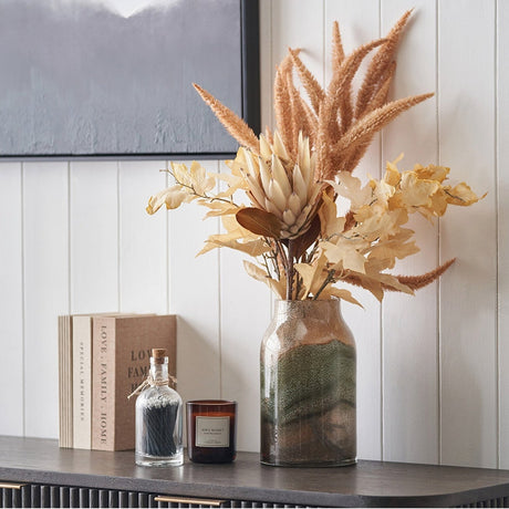 Valtellina Brown & Green Glass Vase, 26cm, with dried pampas grass and foliage stems, styled on a dark sideboard beside books and a candle.